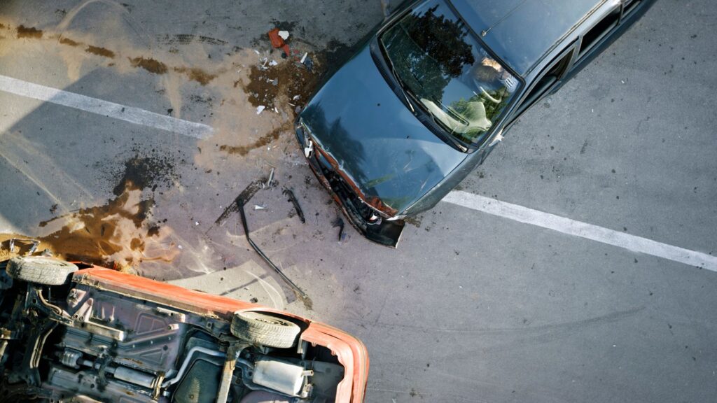 Aerial view of a severe car crash with one vehicle overturned and debris scattered on the road.